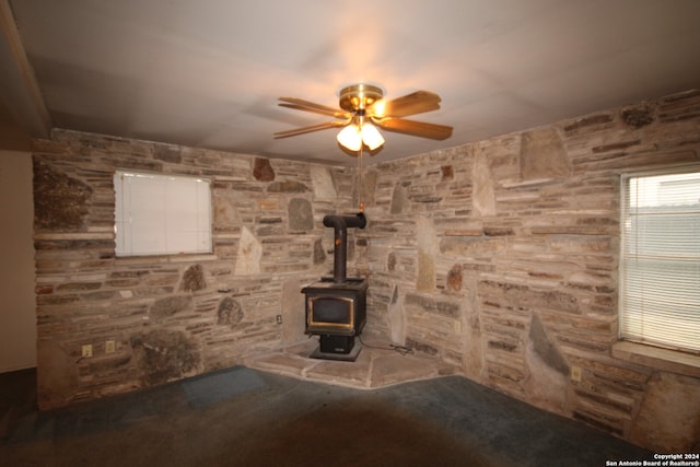 unfurnished living room with ceiling fan and a wood stove