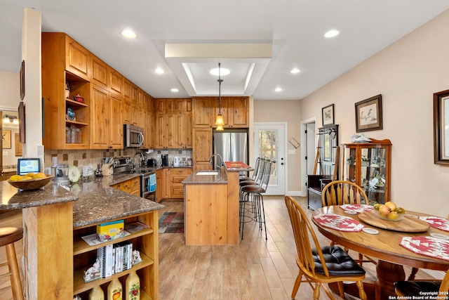 kitchen featuring light hardwood / wood-style floors, stainless steel appliances, backsplash, hanging light fixtures, and a breakfast bar area