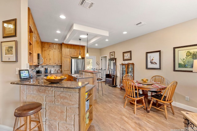 kitchen featuring decorative light fixtures, dark stone countertops, a kitchen breakfast bar, and kitchen peninsula