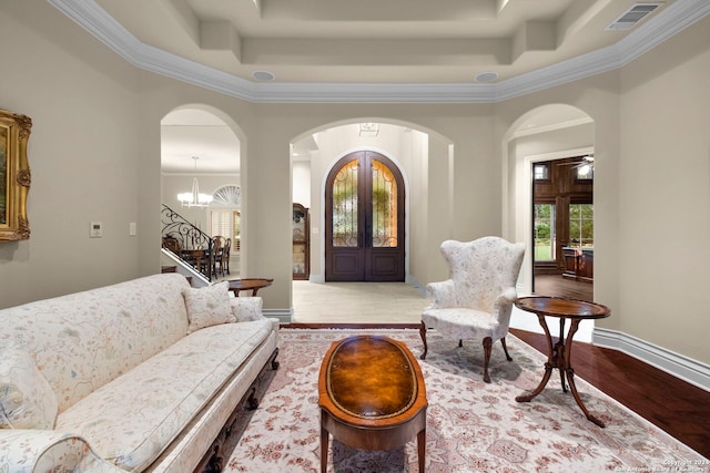 living room with hardwood / wood-style floors, a raised ceiling, an inviting chandelier, and crown molding