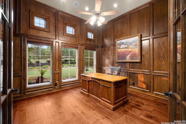 unfurnished office featuring wooden walls, ceiling fan, a towering ceiling, and hardwood / wood-style flooring