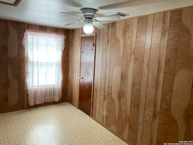 unfurnished room featuring a wealth of natural light, wood walls, and ceiling fan