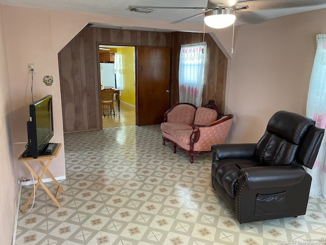 living area with light tile flooring, wooden walls, and ceiling fan