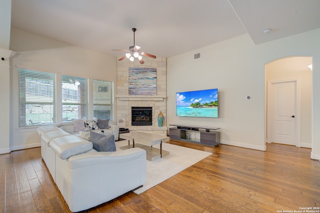 living room featuring a stone fireplace, ceiling fan, vaulted ceiling, and wood-type flooring