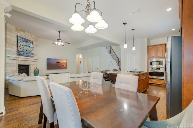 dining room featuring a stone fireplace, hardwood / wood-style flooring, and ceiling fan with notable chandelier