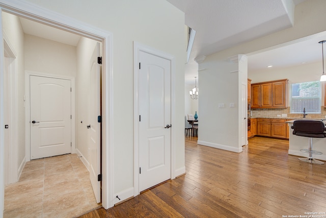 hallway featuring a notable chandelier, ornate columns, sink, and light hardwood / wood-style floors