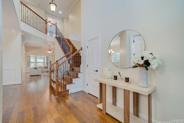 foyer entrance featuring a towering ceiling, decorative columns, ceiling fan with notable chandelier, and hardwood / wood-style floors