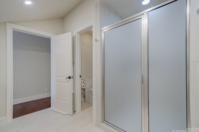 bathroom featuring a shower with door, lofted ceiling, wood-type flooring, and toilet