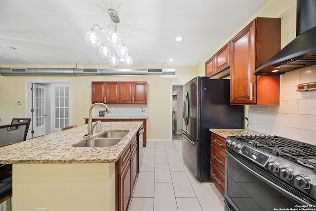 kitchen with wall chimney range hood, black appliances, an island with sink, sink, and pendant lighting