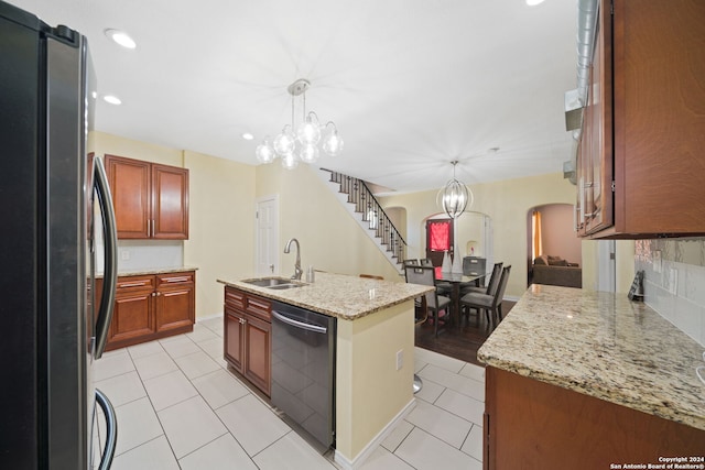 kitchen with stainless steel refrigerator, dishwasher, hanging light fixtures, a kitchen island with sink, and sink