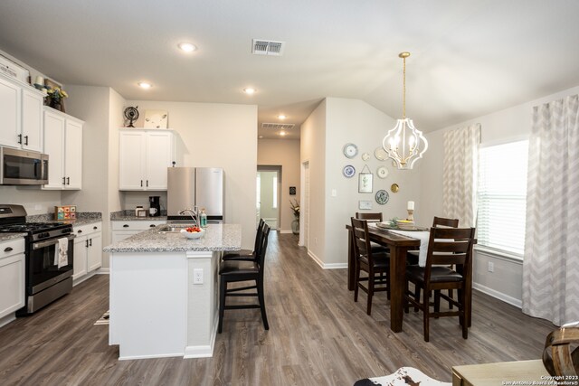 kitchen with decorative light fixtures, stainless steel appliances, a center island with sink, a kitchen bar, and hardwood / wood-style floors