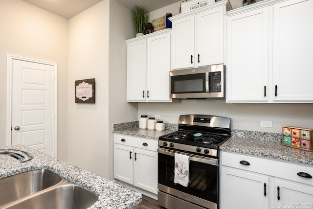 kitchen with light stone countertops, stainless steel appliances, white cabinets, and sink