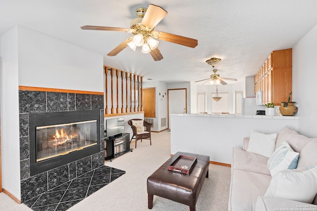 carpeted living room featuring ceiling fan, a tile fireplace, and a textured ceiling