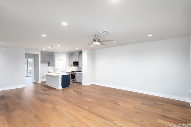 kitchen featuring sink, light hardwood / wood-style flooring, appliances with stainless steel finishes, backsplash, and a center island with sink