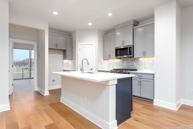 kitchen featuring gray cabinets, sink, decorative backsplash, a center island with sink, and light hardwood / wood-style flooring