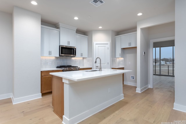 kitchen featuring sink, a kitchen island with sink, white cabinetry, stainless steel appliances, and tasteful backsplash