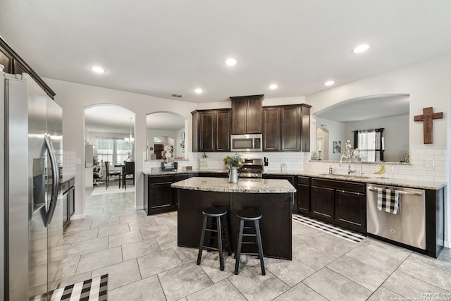 kitchen with dark brown cabinetry, a kitchen island, backsplash, appliances with stainless steel finishes, and sink