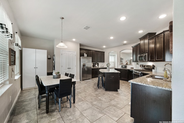 kitchen with stainless steel appliances, pendant lighting, a kitchen island, sink, and a breakfast bar area