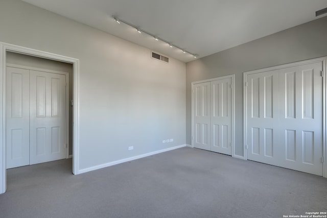 unfurnished bedroom with visible vents, baseboards, carpet, multiple closets, and rail lighting