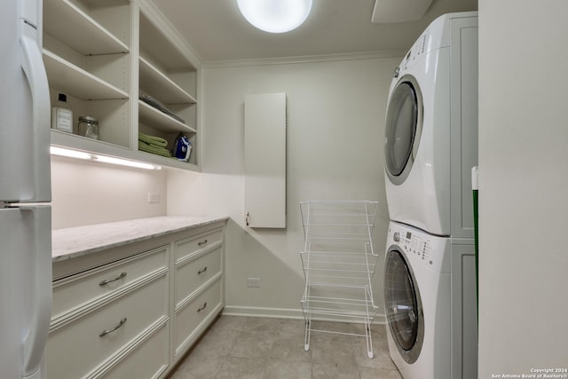 laundry area with light tile patterned floors, baseboards, laundry area, ornamental molding, and stacked washer / dryer