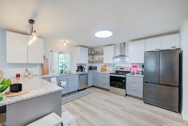 kitchen featuring light hardwood / wood-style flooring, kitchen peninsula, wall chimney exhaust hood, appliances with stainless steel finishes, and pendant lighting