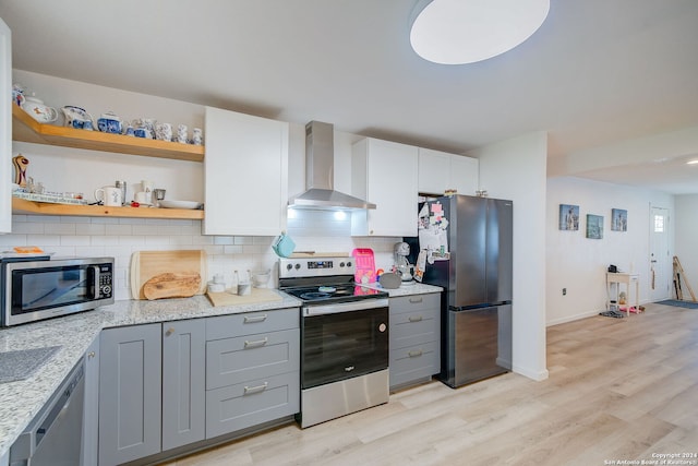 kitchen with light wood-type flooring, stainless steel appliances, white cabinets, wall chimney exhaust hood, and tasteful backsplash