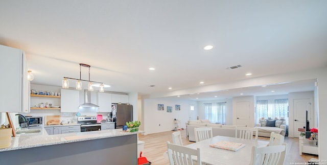 kitchen featuring light hardwood / wood-style flooring, kitchen peninsula, stainless steel appliances, wall chimney exhaust hood, and white cabinetry