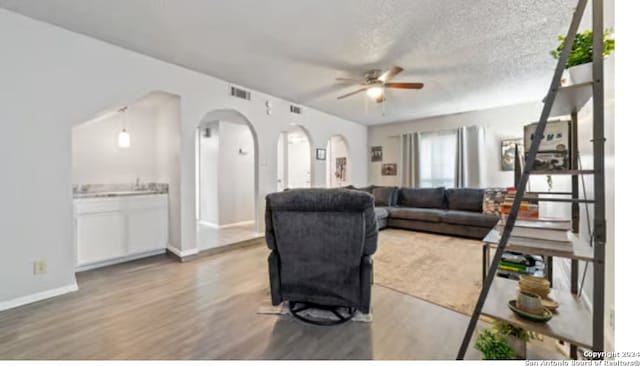 living room with ceiling fan, light hardwood / wood-style flooring, and a textured ceiling