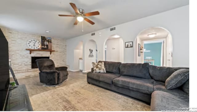 living room featuring wood-type flooring, ceiling fan, a fireplace, and brick wall