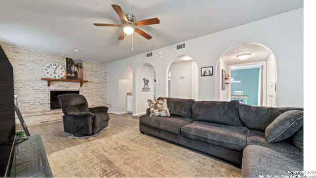 living room with wood-type flooring, ceiling fan, a fireplace, and brick wall