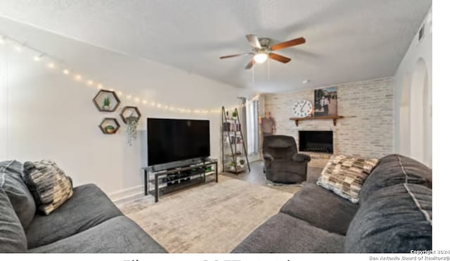 living room with a textured ceiling, ceiling fan, a fireplace, and brick wall