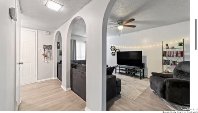 living room featuring ceiling fan, a textured ceiling, and light wood-type flooring