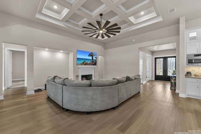 living room featuring french doors, hardwood / wood-style flooring, beam ceiling, a high ceiling, and coffered ceiling