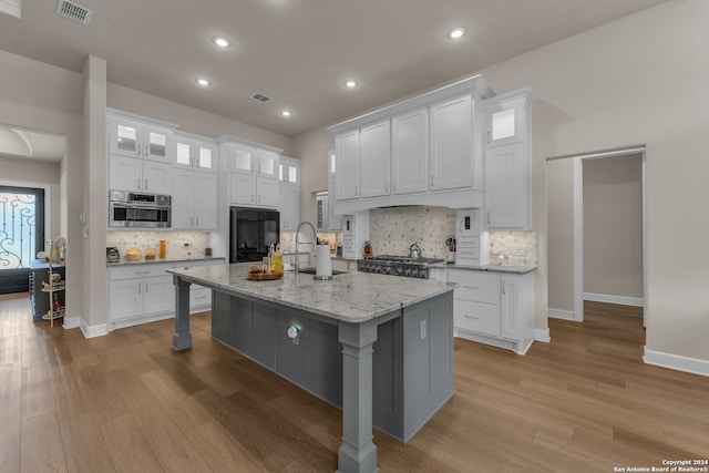 kitchen with white cabinetry, light wood-type flooring, a kitchen island with sink, oven, and tasteful backsplash