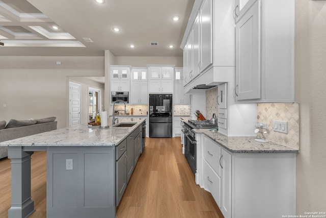 kitchen with coffered ceiling, a center island with sink, beam ceiling, light wood-type flooring, and double oven range