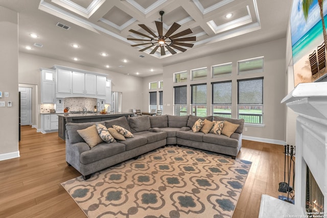 living room featuring coffered ceiling, ornamental molding, beamed ceiling, and light wood-type flooring