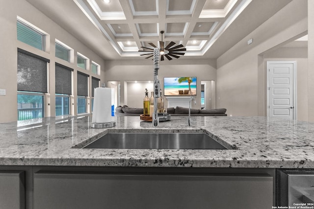 kitchen with beamed ceiling, light stone counters, a high ceiling, coffered ceiling, and ceiling fan