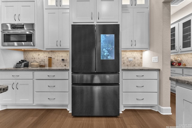 kitchen with white cabinetry, backsplash, black refrigerator, and dark hardwood / wood-style flooring