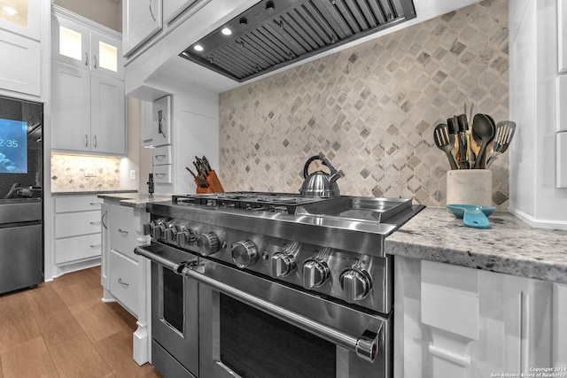 kitchen with custom range hood, light hardwood / wood-style flooring, stainless steel appliances, white cabinets, and backsplash