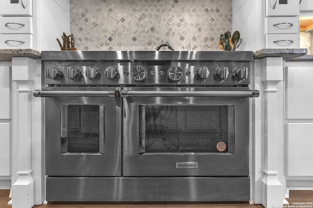 details with stone countertops, hardwood / wood-style flooring, tasteful backsplash, and range with two ovens