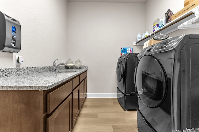 laundry room with sink, light hardwood / wood-style flooring, independent washer and dryer, and cabinets