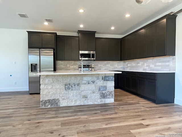 kitchen featuring light wood-type flooring, backsplash, a center island with sink, and appliances with stainless steel finishes