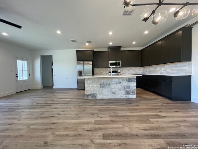 kitchen featuring decorative backsplash, a center island with sink, light hardwood / wood-style flooring, and stainless steel appliances