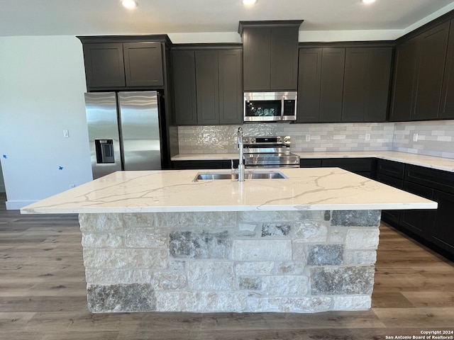 kitchen with hardwood / wood-style flooring, light stone counters, a center island with sink, and appliances with stainless steel finishes