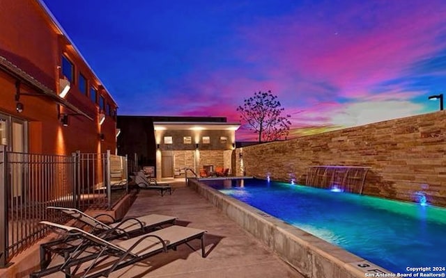 pool at dusk featuring a patio and pool water feature