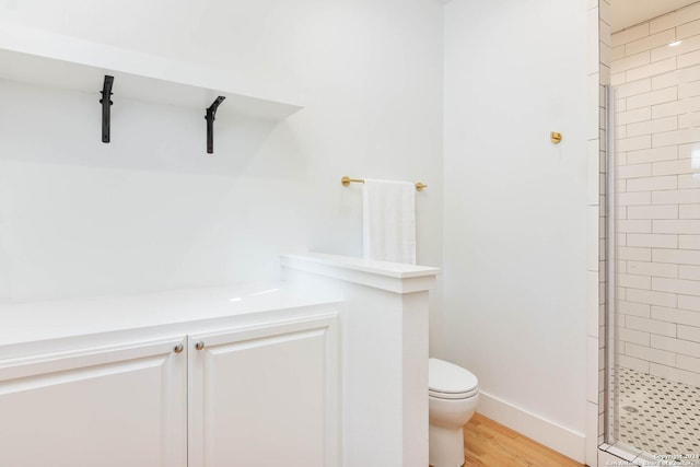 bathroom with tiled shower, hardwood / wood-style floors, and toilet