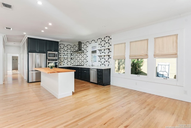 kitchen featuring wall chimney exhaust hood, stainless steel appliances, butcher block countertops, backsplash, and light hardwood / wood-style floors