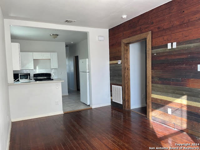 interior space featuring white cabinetry, white refrigerator, light hardwood / wood-style flooring, range, and wood walls