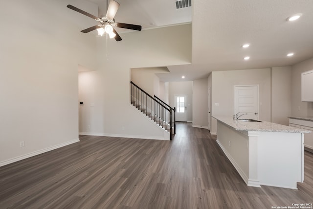 unfurnished living room featuring a sink, visible vents, baseboards, stairs, and dark wood finished floors