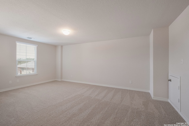 empty room with light carpet, a textured ceiling, visible vents, and baseboards